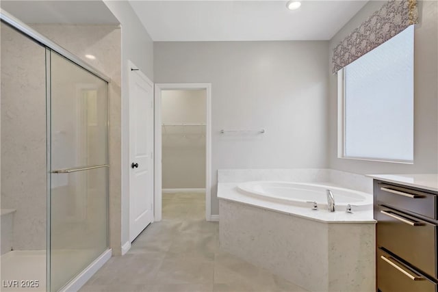 bathroom featuring a stall shower, a garden tub, a walk in closet, and vanity