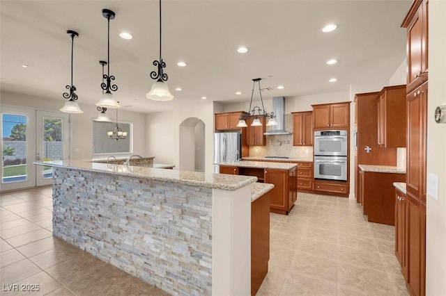 7668 Friendly Breeze Ct, Las Vegas, NV 89123 - kitchen with a large island with sink, appliances with stainless steel finishes, wall chimney range hood, brown cabinets, and backsplash