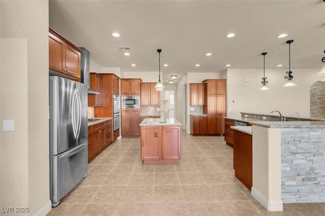 7668 Friendly Breeze Ct, Las Vegas, NV 89123 - kitchen featuring stainless steel appliances, a sink, a center island with sink, wall chimney exhaust hood, and brown cabinetry