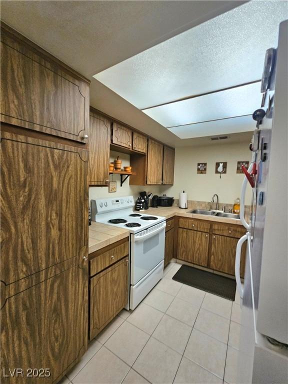 1128 Willow Tree Dr Unit C, Las Vegas, NV 89128 - kitchen with white range with electric stovetop, a sink, light tile patterned floors, brown cabinets, and a textured ceiling