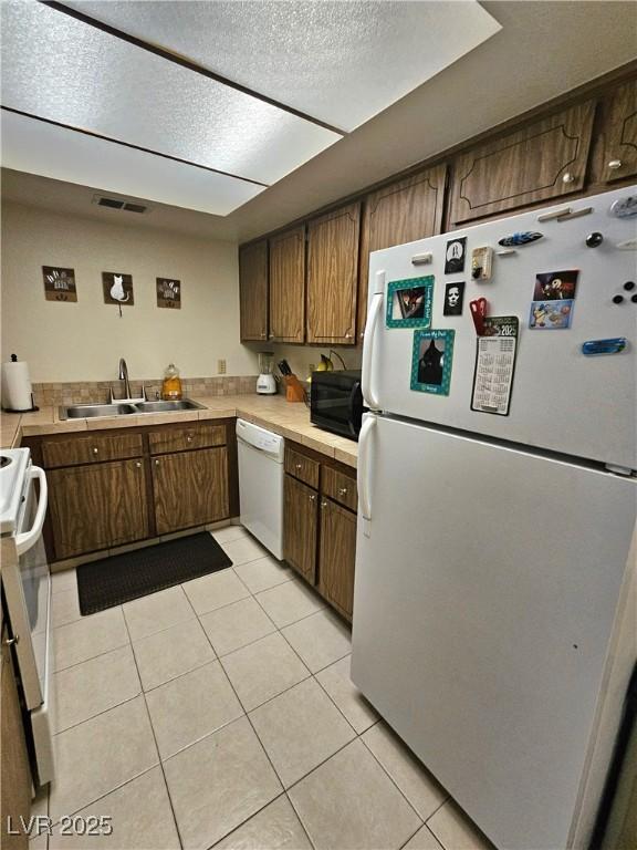 1128 Willow Tree Dr Unit C, Las Vegas, NV 89128 - kitchen with white appliances, a sink, light tile patterned flooring, brown cabinets, and a textured ceiling