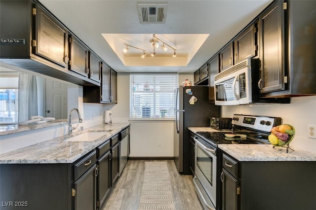kitchen featuring stainless steel appliances, a sink, light wood-style floors, a raised ceiling, and baseboards