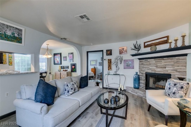 living room with arched walkways, wood finished floors, and a tile fireplace