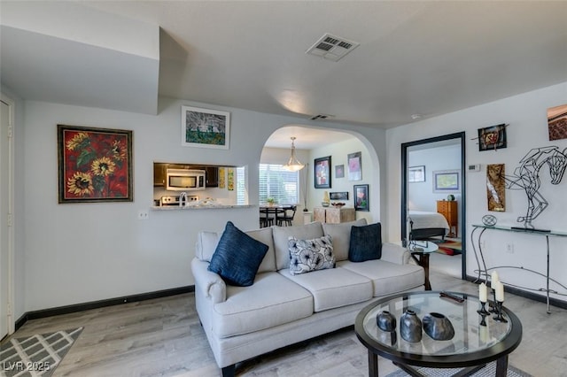 living area with arched walkways, light wood-style flooring, and baseboards
