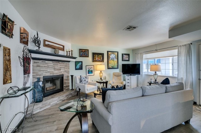 living room featuring a tiled fireplace, wood finished floors, and a textured ceiling