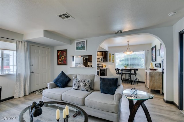 living area featuring arched walkways, light wood-style flooring, and baseboards