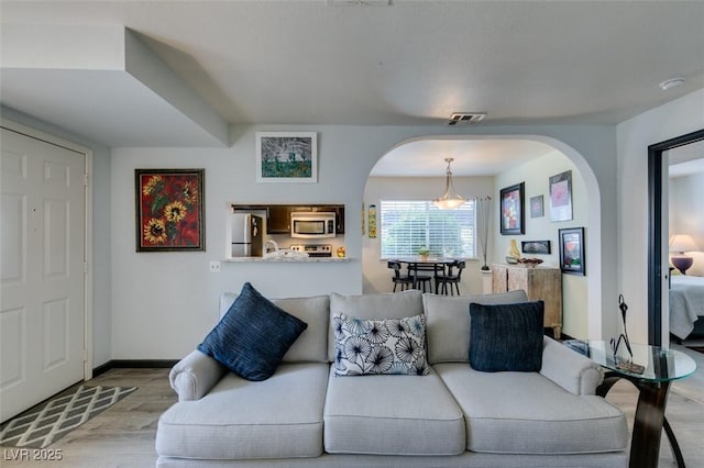 living area with arched walkways, wood finished floors, and baseboards