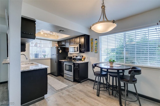 kitchen featuring appliances with stainless steel finishes, a sink, light wood finished floors, baseboards, and light stone countertops