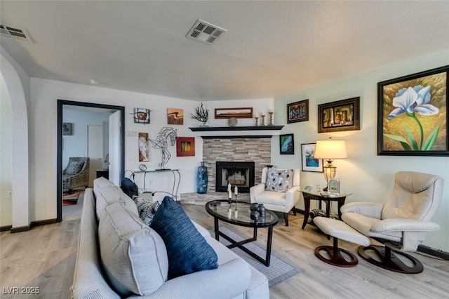 living area featuring light wood-type flooring, a fireplace, baseboards, and arched walkways