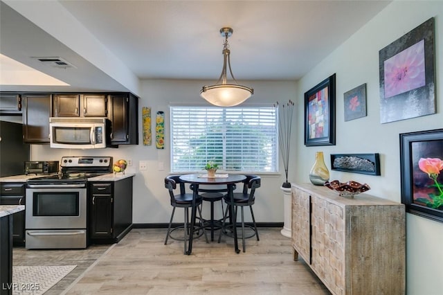 kitchen with stainless steel appliances, light countertops, light wood-style flooring, and hanging light fixtures