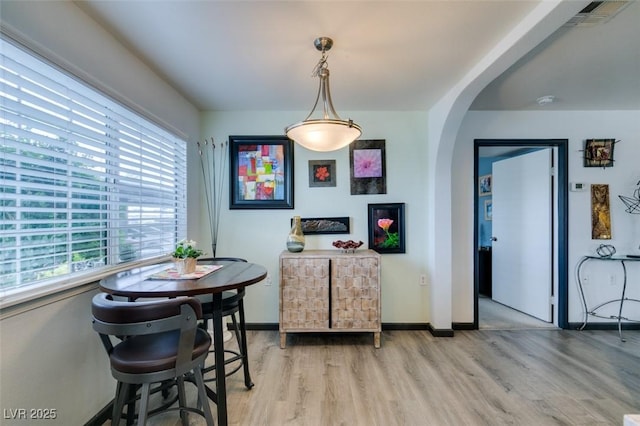 dining area featuring light wood finished floors, arched walkways, and baseboards