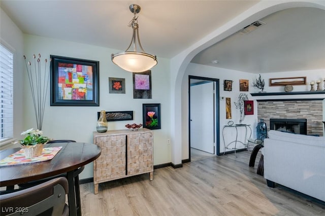 dining space with arched walkways, light wood finished floors, baseboards, and a fireplace
