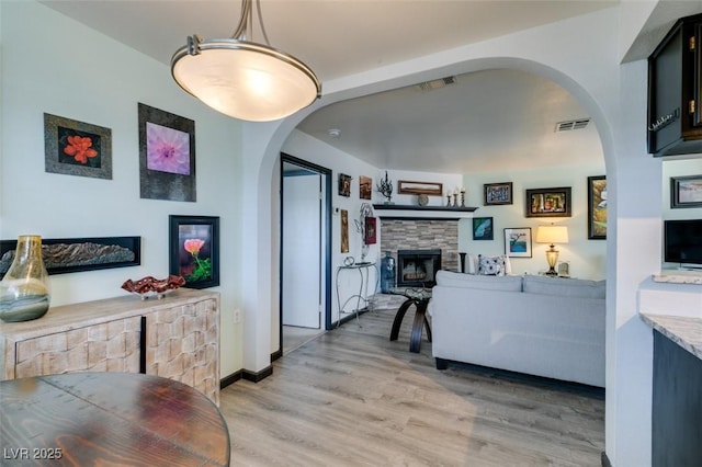living room featuring a fireplace, light wood-style flooring, and arched walkways