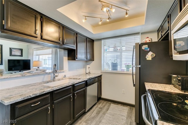 kitchen featuring appliances with stainless steel finishes, a sink, light wood-style floors, a raised ceiling, and baseboards