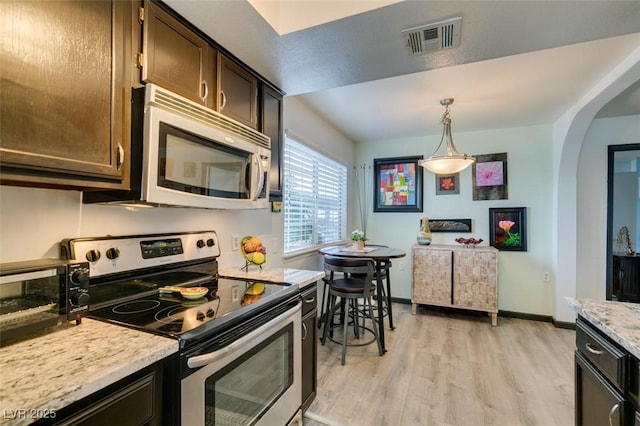 kitchen with stainless steel appliances, light wood finished floors, dark brown cabinets, arched walkways, and pendant lighting