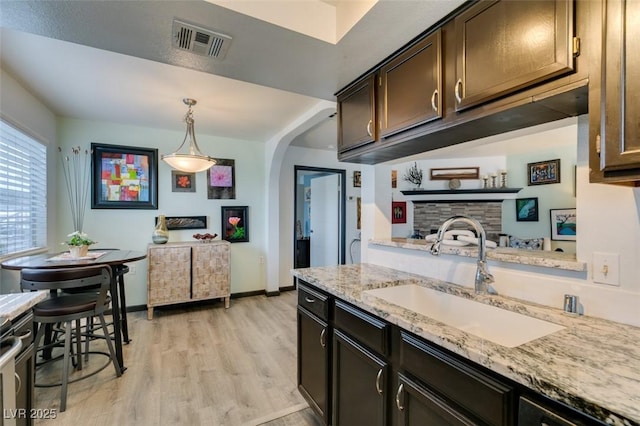kitchen featuring a sink, light wood-type flooring, arched walkways, light stone counters, and pendant lighting
