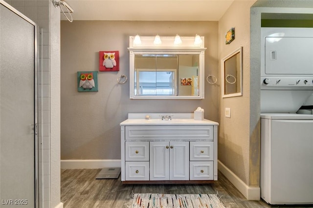 bathroom with estacked washer and dryer, wood finished floors, baseboards, and a shower with door