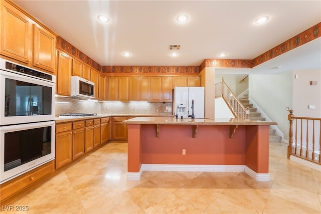 395 Suzanne Peak Ct, Henderson, NV 89012 - kitchen with white appliances, backsplash, light stone countertops, a spacious island, and a breakfast bar