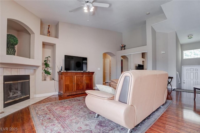 5000 Red Rock St Unit 237, Las Vegas, NV 89118 - living room featuring a ceiling fan, wood finished floors, a tiled fireplace, arched walkways, and baseboards