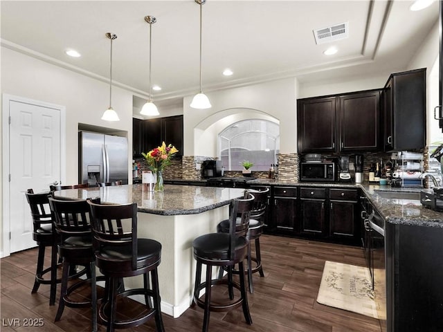 6465 Grande River Ct, Las Vegas, NV 89139 - kitchen featuring appliances with stainless steel finishes, dark stone counters, a kitchen bar, decorative backsplash, and dark wood finished floors