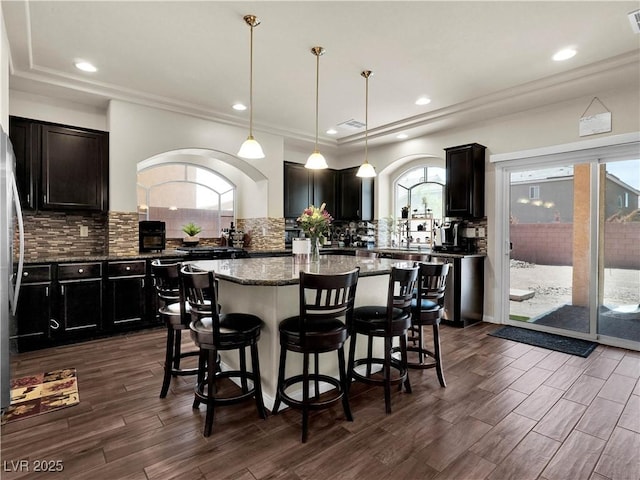 6465 Grande River Ct, Las Vegas, NV 89139 - kitchen featuring a center island, a kitchen breakfast bar, tasteful backsplash, dark stone countertops, and dark wood-type flooring