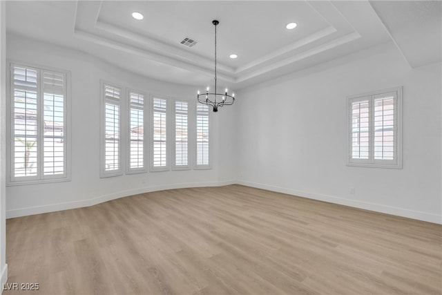 unfurnished room featuring a tray ceiling, plenty of natural light, a chandelier, light wood-style floors, and recessed lighting