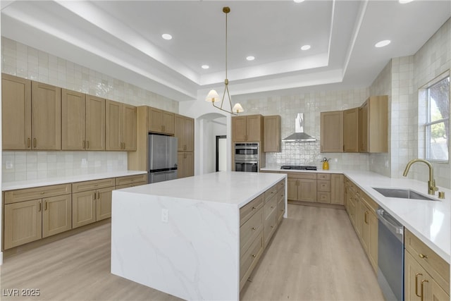 kitchen with stainless steel appliances, a sink, a center island, wall chimney exhaust hood, and light wood-type flooring