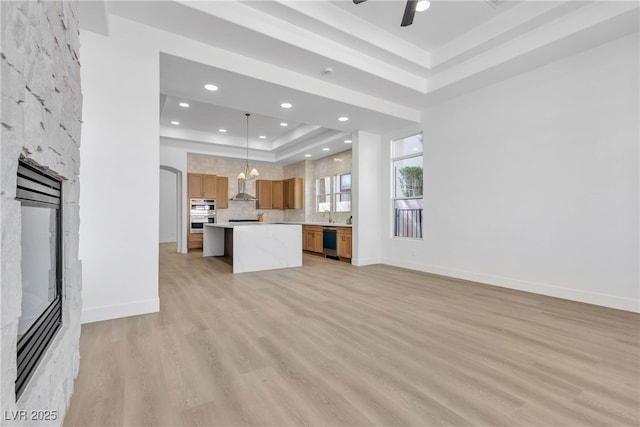 unfurnished living room with a raised ceiling, a fireplace, light wood finished floors, a ceiling fan, and recessed lighting