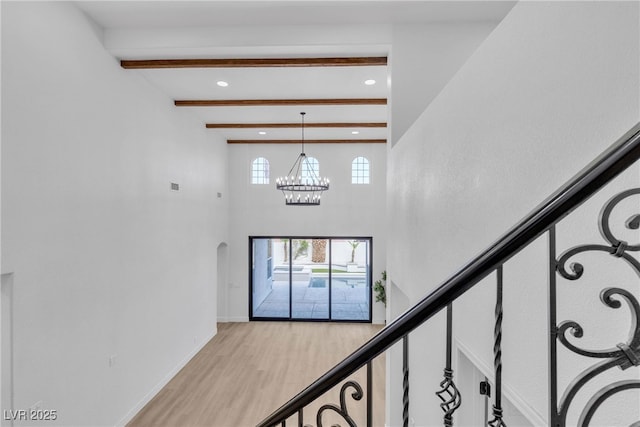foyer with beam ceiling, wood finished floors, a chandelier, recessed lighting, and arched walkways