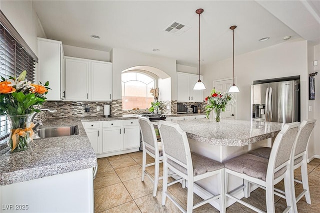 6409 Shawnee Springs Ct, Las Vegas, NV 89139 - kitchen with decorative backsplash, stainless steel fridge, a breakfast bar area, white cabinetry, and a center island