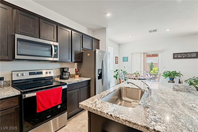 3543 E Malheur Ave, Pahrump, NV 89061 - kitchen with appliances with stainless steel finishes, a sink, dark brown cabinetry, light stone counters, and light tile patterned floors