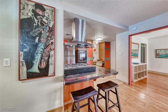 1721 E Oakey Blvd, Las Vegas, NV 89104 - kitchen with island exhaust hood, light wood-type flooring, a textured ceiling, and a breakfast bar