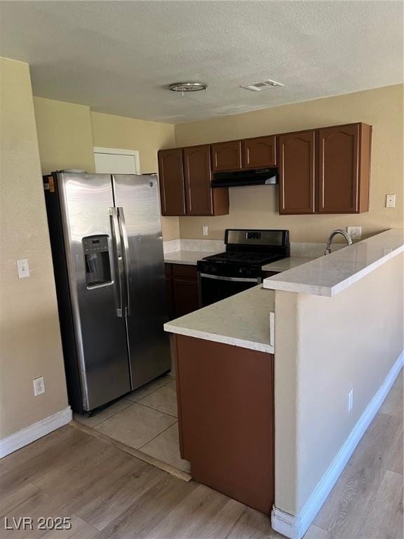 kitchen with black gas range, stainless steel refrigerator with ice dispenser, a peninsula, under cabinet range hood, and light countertops