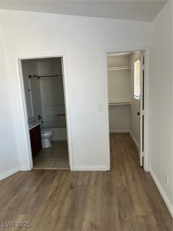 unfurnished bedroom featuring a spacious closet, baseboards, and light wood-type flooring
