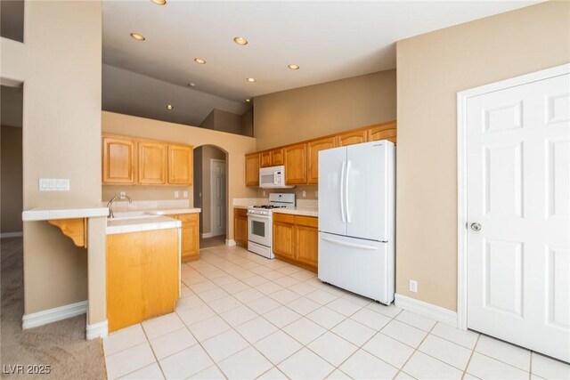 8205 Harrogate Ave, Las Vegas, NV 89129 - kitchen featuring white appliances, vaulted ceiling, a peninsula, tile counters, and arched walkways