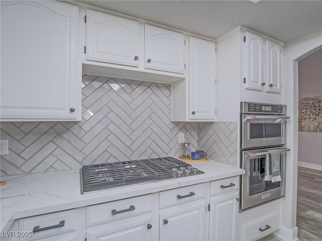 5452 Big Sky Ln, Las Vegas, NV 89149 - kitchen featuring appliances with stainless steel finishes, tasteful backsplash, white cabinetry, arched walkways, and light stone countertops