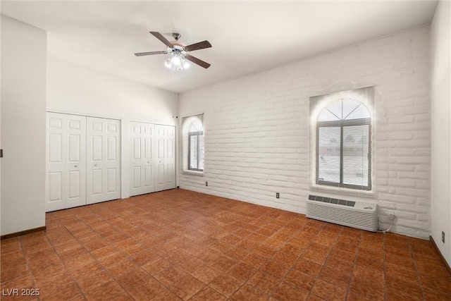 1320 Daytona St, Pahrump, NV 89048 - unfurnished bedroom with two closets, brick wall, an AC wall unit, a ceiling fan, and tile patterned floors