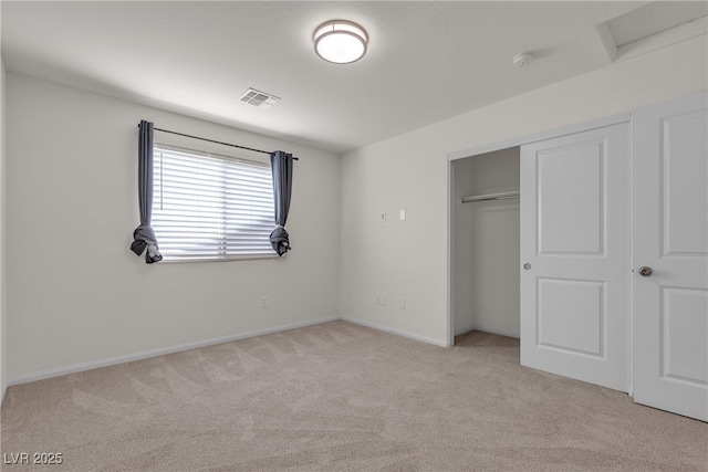 unfurnished bedroom with light colored carpet, a closet, baseboards, and attic access