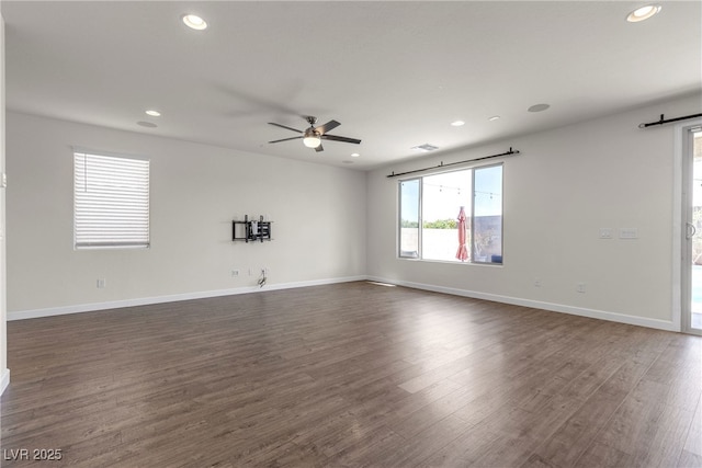 empty room with recessed lighting, dark wood finished floors, ceiling fan, baseboards, and a barn door