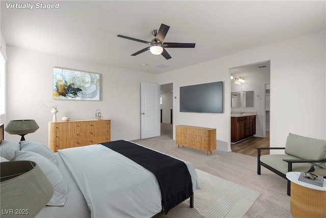 bedroom featuring light carpet, ensuite bath, ceiling fan, and baseboards