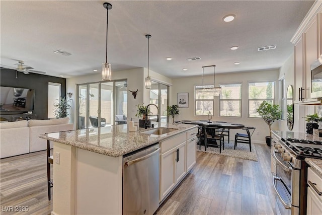 8335 Beaten Path Ct, Las Vegas, NV 89166 - kitchen featuring a sink, appliances with stainless steel finishes, light wood finished floors, a center island with sink, and white cabinetry