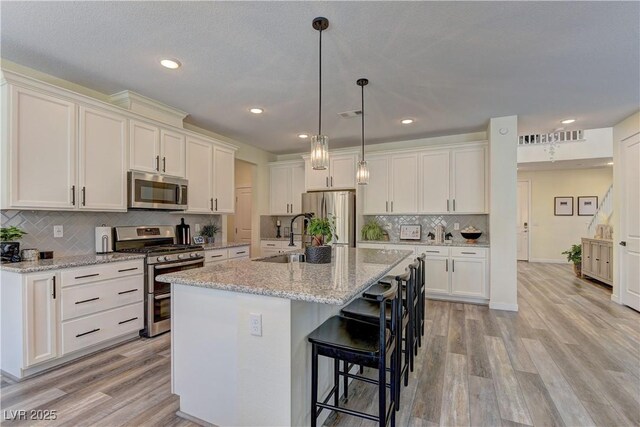 8335 Beaten Path Ct, Las Vegas, NV 89166 - kitchen featuring appliances with stainless steel finishes, a sink, white cabinetry, light wood finished floors, and a center island with sink