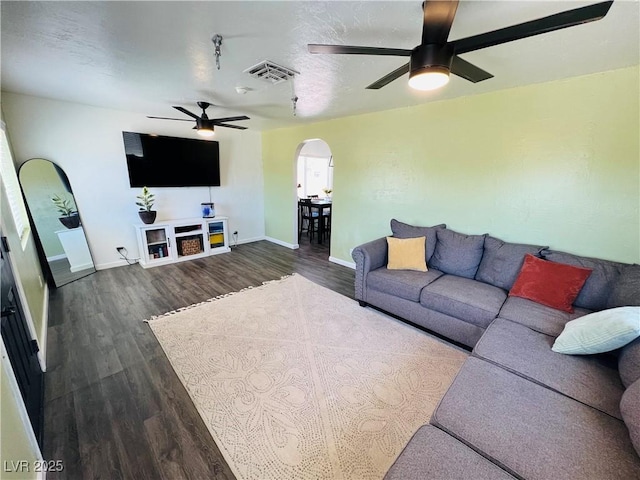 living area featuring a ceiling fan, arched walkways, dark wood finished floors, and baseboards