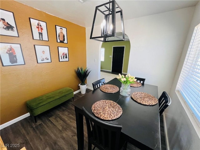 dining room with wood finished floors, arched walkways, and baseboards
