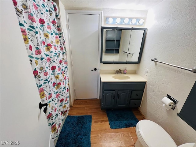 bathroom with a textured wall, wood finished floors, vanity, toilet, and a shower with shower curtain