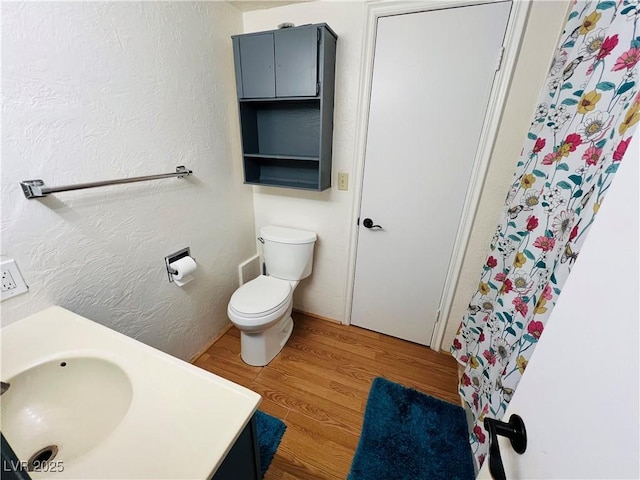full bathroom with toilet, a textured wall, wood finished floors, and vanity