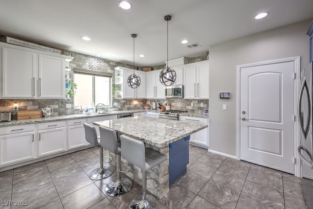10623 Auburn Springs Ave, Las Vegas, NV 89166 - kitchen featuring stainless steel appliances, backsplash, white cabinets, a kitchen island, and decorative light fixtures