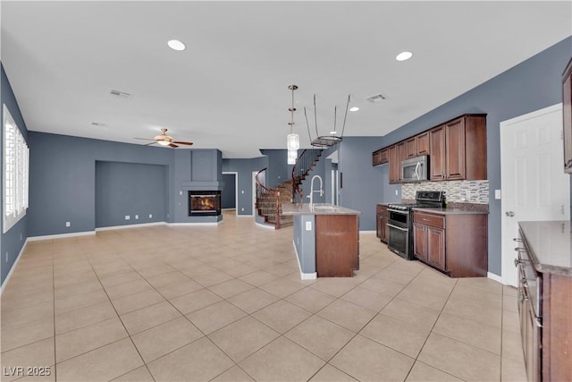4063 Lower Saxon Ave, North Las Vegas, NV 89085 - kitchen with stainless steel appliances, a glass covered fireplace, a ceiling fan, open floor plan, and backsplash