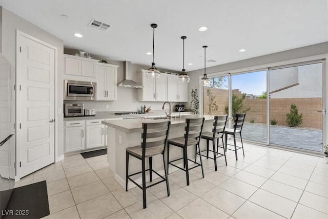 10324 Stroma Ave, Las Vegas, NV 89166 - kitchen featuring wall chimney exhaust hood, stainless steel microwave, a kitchen bar, white cabinetry, and a kitchen island with sink