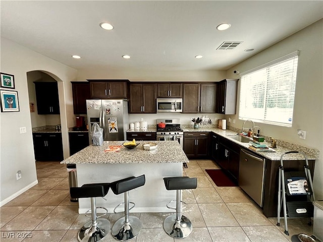 kitchen featuring stainless steel appliances, a sink, a kitchen island, light stone countertops, and arched walkways